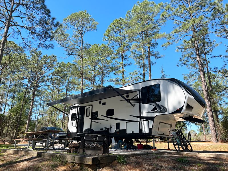 A fifth wheel RV parked at a campsite in the woods.